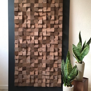 Puede incluir: Una gran pieza de arte de pared de madera hecha de cuadrados individuales, cada uno con una textura y un patr&oacute;n de veta &uacute;nicos. Los cuadrados est&aacute;n dispuestos en un patr&oacute;n geom&eacute;trico, creando un dise&ntilde;o moderno y abstracto. El arte de pared est&aacute; montado en un marco negro y se muestra contra una pared blanca.