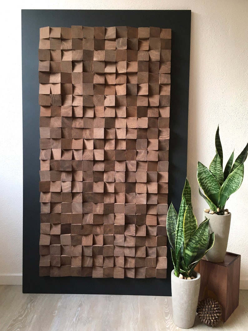 Puede incluir: Una gran pieza de arte de pared de madera hecha de cuadrados individuales, cada uno con una textura y un patr&oacute;n de veta &uacute;nicos. Los cuadrados est&aacute;n dispuestos en un patr&oacute;n geom&eacute;trico, creando un dise&ntilde;o moderno y abstracto. El arte de pared est&aacute; montado en un marco negro y se muestra contra una pared blanca.