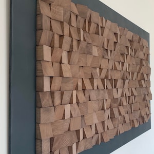 Puede incluir: Una pieza de arte de pared hecha de madera con un marco gris oscuro. La madera est&aacute; dispuesta en un patr&oacute;n geom&eacute;trico, creando un aspecto texturizado y moderno.
