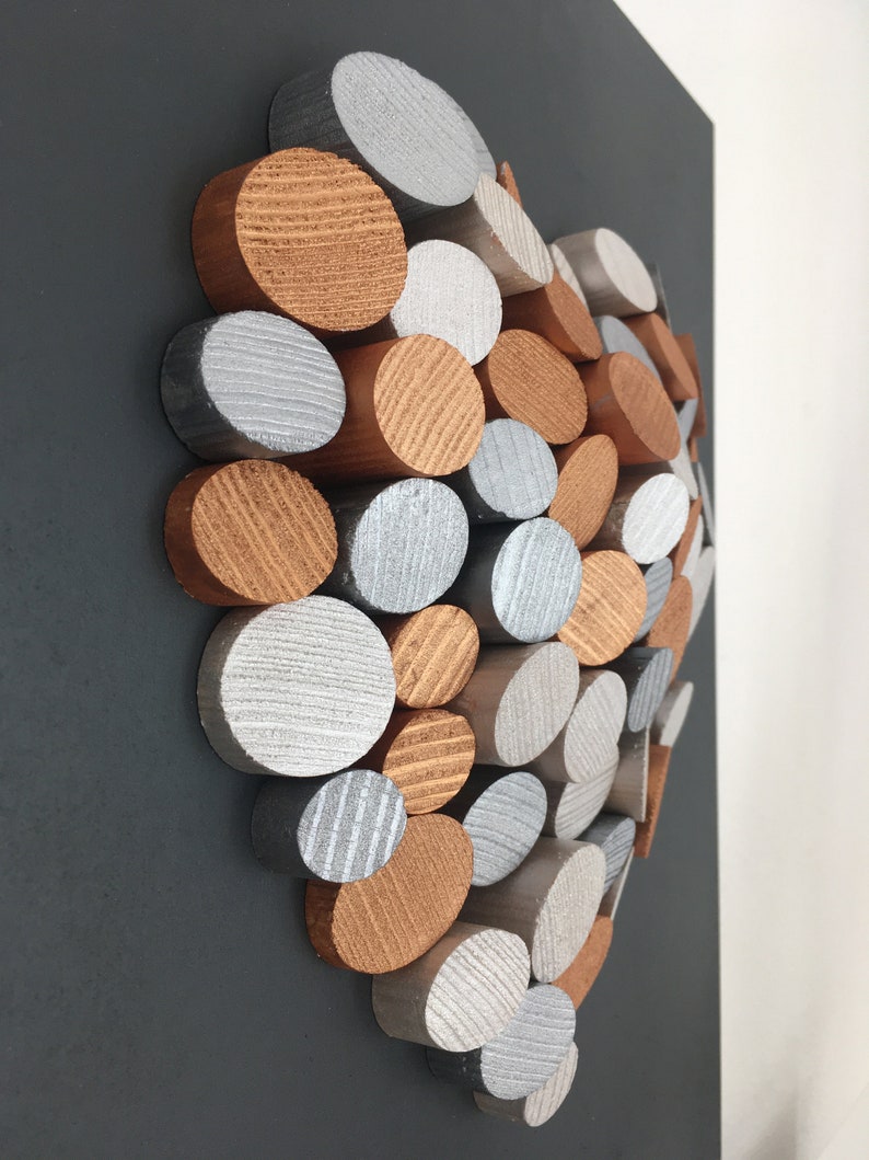 May include: A heart-shaped wall art piece made of wood circles in silver and copper tones. The circles are arranged in a random pattern, creating a unique and modern design.