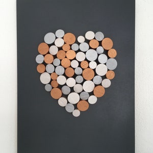 May include: A heart-shaped wall art piece made of wood rounds in shades of silver, white, and copper. The rounds are arranged in a heart shape on a black background.