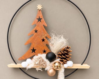 May include: A black metal hoop wreath featuring a rust-colored metal Christmas tree with star cutouts, a wooden star topper, a pinecone, a matte black ornament, two gold-toned ornaments, white pom-poms, and fibrous beige filler material.