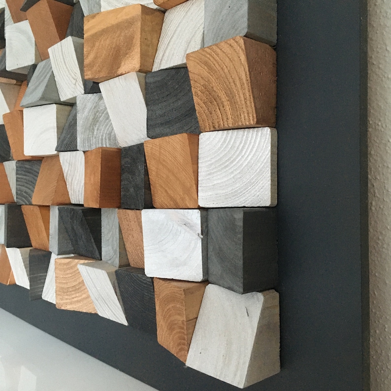 May include: A wall art piece made of wood blocks in various shades of gray, white, and brown. The blocks are arranged in a geometric pattern and are mounted on a black background.