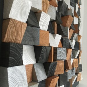 May include: A geometric wall art piece made of wood blocks in various shades of gray, white, and brown. The blocks are arranged in a pattern of triangles and squares.