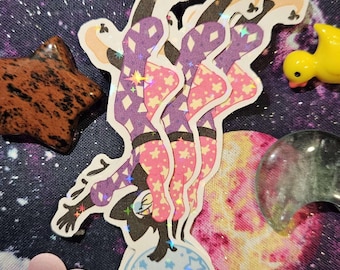 May include: A holographic sticker of a cartoon character in a purple and pink outfit balancing on a blue and white ball with stars. The character has black hair and a black mask.