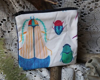 May include: A small, rectangular fabric zip pouch featuring a white background with a colourful print of various beetles. The largest beetle has orange and blue wings with teal accents, while smaller beetles are coloured in shades of red, blue, and green.