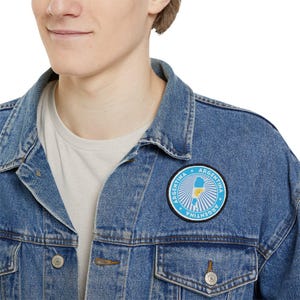 May include: A blue denim jacket with a circular patch featuring a white outline of Argentina with the words "Argentina" in white text.