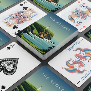 Pode incluir: Um baralho de cartas com um design de paisagem com um farol e o texto "THE AZORES" nas costas das cartas. As cartas são cercadas por outras cartas de jogar, incluindo um Rei de Paus, um Ás de Espadas e curingas.