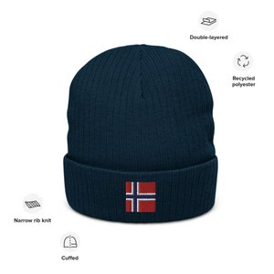 May include: A navy blue knitted beanie with a cuffed brim and a small embroidered Norwegian flag on the front. The beanie is made from recycled polyester and is double-layered for warmth.