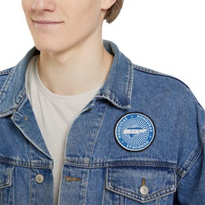 May include: A blue denim jacket with a circular patch featuring the words "Honduras" and a stylized map of Honduras with the Honduran flag colors.