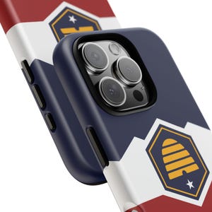 Puede incluir: Una funda de teléfono azul y blanca con un diseño rojo, blanco y azul. La funda presenta un logotipo de colmena con una estrella en el centro. La funda está diseñada para un teléfono con una lente de cámara triple.