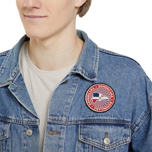 May include: A blue denim jacket with a red, white and blue circular patch that says "Dominicana" in a white circle with a black outline. The patch features a stylised image of the Dominican Republic.
