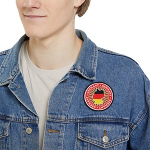 May include: A blue denim jacket with a red, yellow, and black circular patch that says "Germany" in a circle around the outline of Germany with the German flag colors inside.