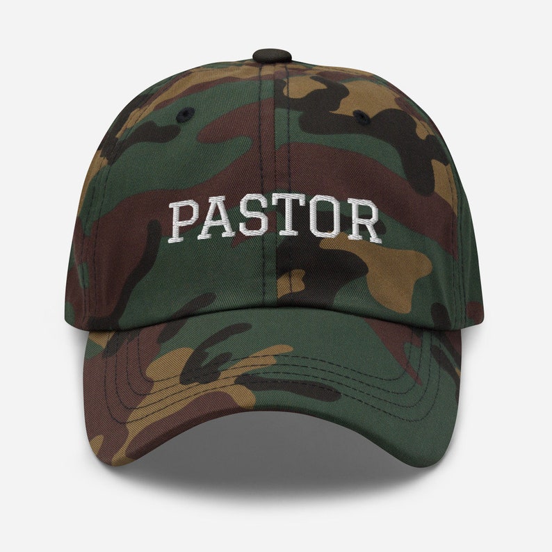 May include: A camouflage baseball cap with the word "PASTOR" embroidered in white on the front.