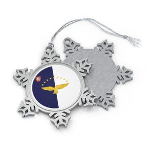 May include: A silver snowflake Christmas ornament with a circular image of the flag of the Azores. The flag is blue and white with a yellow bird.
