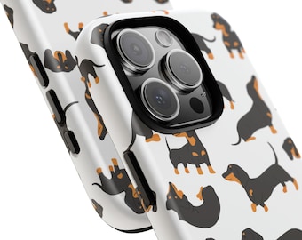 Könnte beinhalten: Eine weiße iPhone-Hülle mit einem schwarzen Kameraobjektiv und einem Muster aus schwarzen und braunen Dackeln.