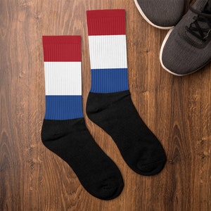 Puede incluir: Un par de calcetines negros con rayas rojas, blancas y azules, que se asemejan a la bandera holandesa.