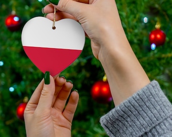 Może przedstawiać: Ręka trzyma ozdobę w kształcie serca z kolorami polskiej flagi, czerwonym i białym, na tle zielonej choinki.