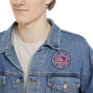 May include: A blue denim jacket with a circular patch featuring the outline of Haiti with the Haitian flag colors and the word "Haiti" repeated around the edge.