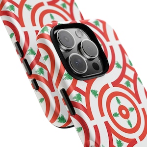 May include: A white phone case with a repeating pattern of red arches and green cedar trees. The phone case has a black camera housing and buttons. The design is a nod to the Lebanese flag.