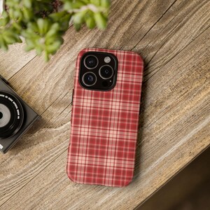 May include: A red and white plaid phone case with a black camera bump. The case is designed for a smartphone with a triple camera system.