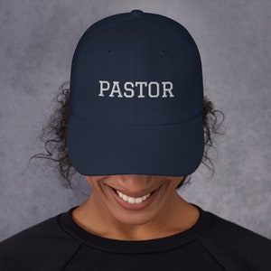 May include: A navy blue baseball cap with white embroidered text that reads "PASTOR".