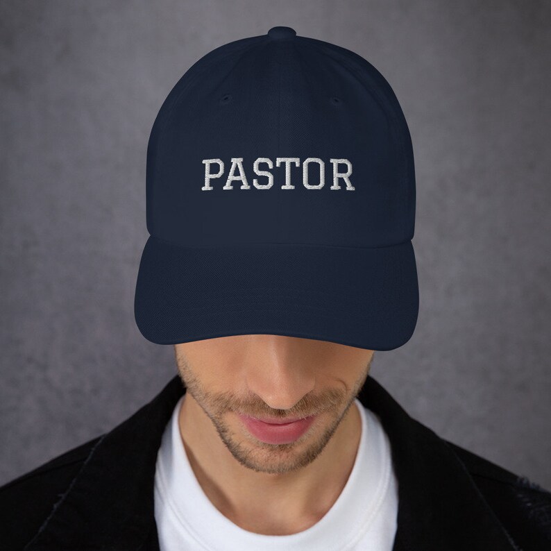 May include: A navy blue baseball cap with white embroidered text that reads "PASTOR".