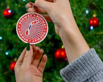 May include: A red and blue Christmas ornament with a white outline and the word "NORWAY" repeated around the edge. The ornament features a stylized map of Norway with a red, white, and blue color scheme.