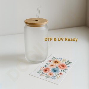 May include: A frosted glass can-shaped tumbler with a bamboo lid and a clear glass straw. A floral design card with peach, blue, and yellow flowers is next to the tumbler. The text "DTF & UV Ready" is printed on the glass.