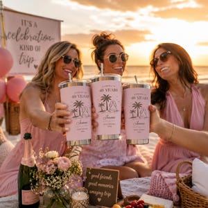 May include: Three pink insulated tumblers with silver lids are held up in a toast. Each tumbler has the text "Cheers to 40 Years" and a beach scene. The tumblers are personalized with the name "Joanne" and the location "Gulf Shores 2024".