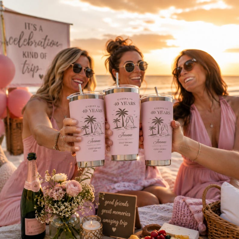 May include: Three pink insulated tumblers with silver lids are held up in a toast. Each tumbler has the text "Cheers to 40 Years" and a beach scene. The tumblers are personalized with the name "Joanne" and the location "Gulf Shores 2024".