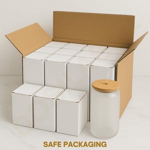 May include: A cardboard box filled with white boxes, and a single frosted glass tumbler with a bamboo lid and straw. The text "SAFE PACKAGING" is printed in gold at the bottom of the image. The tumbler is designed for cold beverages.
