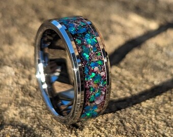 May include: A silver ring with a band of iridescent green, blue, and pink glitter embedded in the metal.