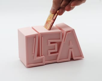 Può includere: Salvadanaio rosa a forma del nome "LEA" con una banconota in euro inserita nella fessura.