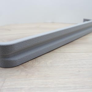 May include: A gray, textured, rectangular object with rounded corners. The object has a grooved design and appears to be made of a solid material. The item is likely a furniture component or decorative element.