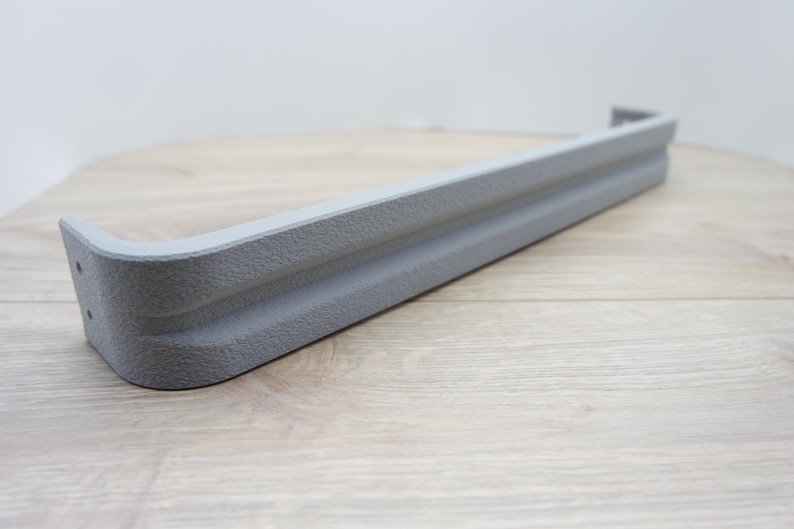 May include: A gray, textured, rectangular object with rounded corners. The object has a grooved design and appears to be made of a solid material. The item is likely a furniture component or decorative element.