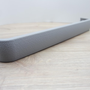 May include: A gray, textured plastic automotive interior trim piece. The trim has a rectangular shape with a curved end and a small, raised edge. The piece is approximately 12 inches long.