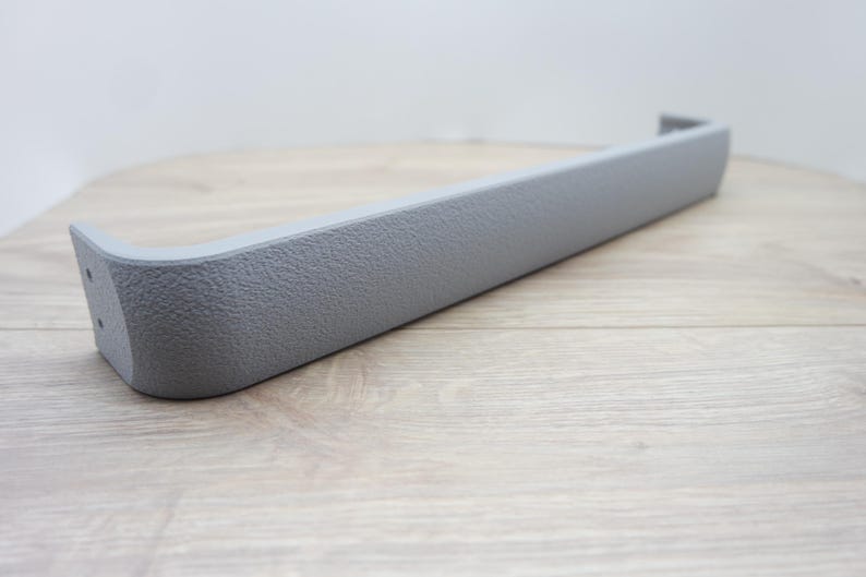 May include: A gray, textured plastic automotive interior trim piece. The trim has a rectangular shape with a curved end and a small, raised edge. The piece is approximately 12 inches long.
