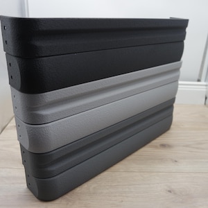 May include: A stack of four collapsible, textured plastic containers in shades of gray and black. The containers are stacked on top of each other, with the top one being black, followed by dark gray, light gray, and a darker gray at the bottom.