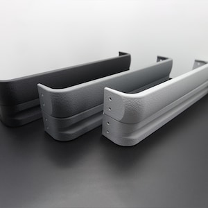 May include: Three textured, curved, rectangular objects in shades of gray, arranged side-by-side. The objects have a layered design with rounded corners and small holes. The colors range from dark gray to light gray.