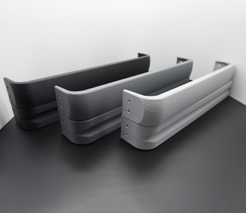 May include: Three textured, curved, rectangular objects in shades of gray, arranged side-by-side. The objects have a layered design with rounded corners and small holes. The colors range from dark gray to light gray.