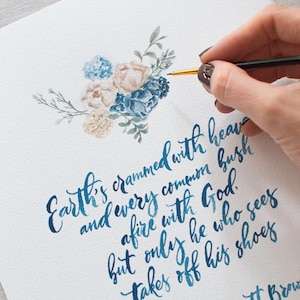 May include: Watercolor artwork featuring a floral arrangement in shades of blue and beige. The artwork includes a handwritten quote in blue ink: "Earth's crammed with heaven..." by Elizabeth Barrett Browning. The artwork is on white paper.