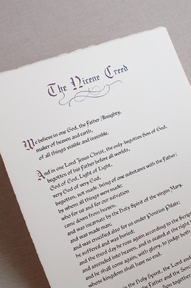 May include: A printed document featuring the text "The Nicene Creed" in elegant calligraphy. The text is in dark purple ink on a white paper with a deckled edge. The document is a religious item.