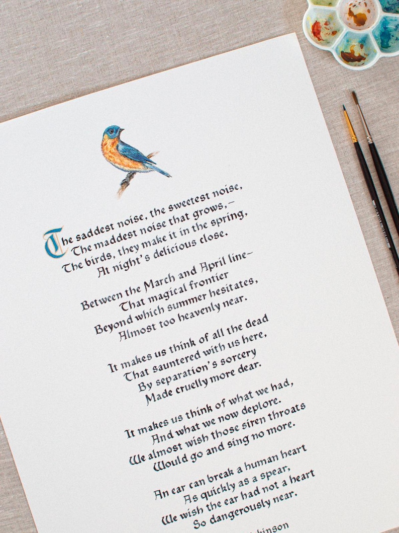 May include: A watercolor print of a poem with a bluebird illustration. The poem is written in elegant calligraphy with a decorative initial letter. Paintbrushes and a paint palette are in the background.