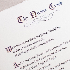 May include: A close-up of a cream-colored paper with the text "The Nicene Creed" in elegant calligraphy. The text is in dark purple and brown ink, with decorative flourishes. The paper has a torn edge.