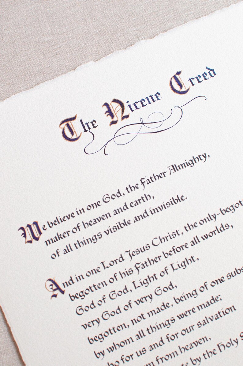 May include: A close-up of a cream-colored paper with the text "The Nicene Creed" in elegant calligraphy. The text is in dark purple and brown ink, with decorative flourishes. The paper has a torn edge.