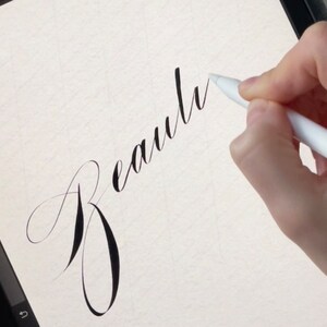 May include: A close-up of a hand writing the word "Beauty" in cursive on a digital tablet using a white stylus.