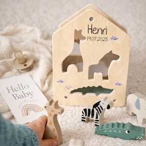 Può includere: Set di giocattoli per bambini in legno. Include un puzzle a forma di casa con ritagli di animali e figure di animali in legno abbinate. La casa è personalizzata con un nome e una data. Include una carta con scritto "Hello Baby".