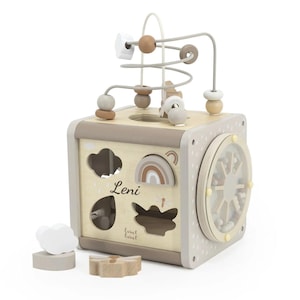 Può includere: Un cubo attività in legno per bambini, con labirinto di perline, classificazione di forme e ruota girevole. Il cubo è dipinto in tonalità neutre con un design arcobaleno e nuvola. Il nome "Leni" è stampato. Include forme in legno.