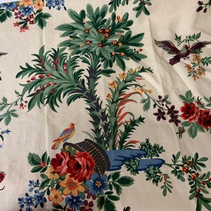 May include: White fabric with a floral pattern featuring green leaves, red, yellow, and blue flowers, and birds. The fabric also has a blue and green bird in a basket.